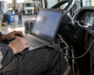 Techniker mit Laptop im Lkw-Fahrerhaus, ein Kabel führt zur Armaturenkonsole